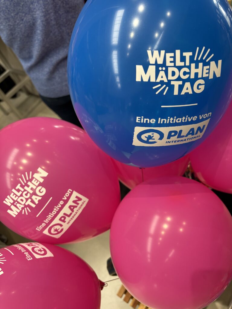 Strahlend blaue und rosa Luftballons mit der Aufschrift Welt-Mädchentag und dem Logo von Plan International.